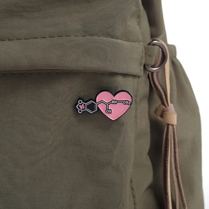 Dettaglio macro di una spilla a cuore rosa con molecola chimica su borsa di tela verde