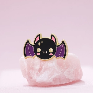 Detailed view of punk bat kitten enamel pin with gold edging on pink crystal base