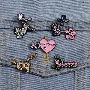 Dettaglio di cinque spille smaltate a molecola chimica con cuori e fiori su denim blu