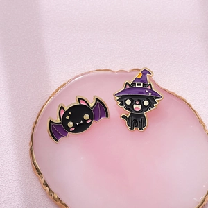 Close-up of cute Halloween bat and wizard cat enamel pins on a pink display plate