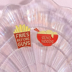 Close-up of enamel pins showing red fries box and noodle bowl on a pearlescent tray