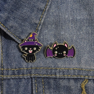 Detailed close-up of cute Halloween cat and bat enamel pins on blue denim fabric background