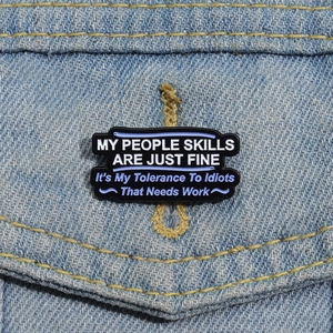 Detail of funny enamel pin with humorous social skills quote on a denim jacket pocket