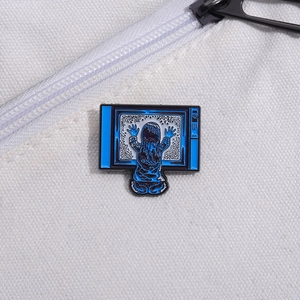 Detail of blue horror movie enamel pin featuring a girl touching a snowy TV screen
