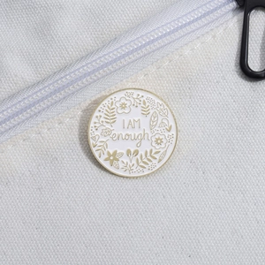 Close-up of circular enamel pin with I AM enough quote and gold floral details