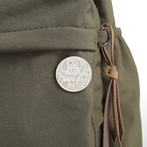 Detailed view of 'I AM enough' enamel pin attached to an olive green canvas fabric