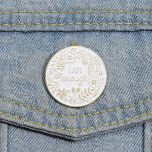 Detail of 'I AM enough' white enamel pin pinned to a blue denim jacket pocket