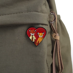 Detail of red heart-shaped fox enamel pin attached to a green canvas backpack