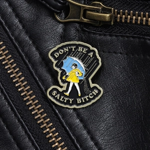 Detail einer Emaille-Brosche mit Regenmädchen und sarkastischem Spruch auf Lederjacke