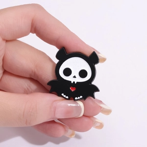 Vue macro d'un pin's tête de chauve-souris avec cœur rouge, tenu par la main