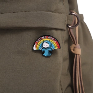 Close-up of enamel grim reaper pin with rainbow and You Are Next text on a green backpack