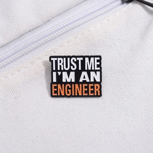 Macro detail of Trust Me I'm an Engineer enamel pin on white fabric texture