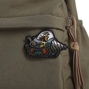 Macro shot of a pixel art metal tank brooch attached to a green nylon backpack