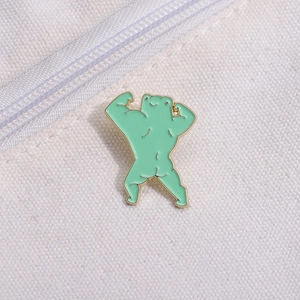 Creative green muscular frog enamel pin displayed on a white canvas bag accessory