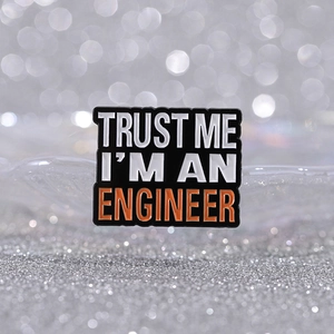 Trust Me I'm An Engineer enamel brooch pin with orange text on silver bokeh background