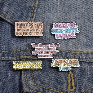 Set mit fünf bunten Emaille-Pins mit motivierenden Zitaten auf blauem Denim-Stoff