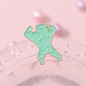 Funny muscular cartoon frog enamel brooch with gold metal base on a pink aesthetic background