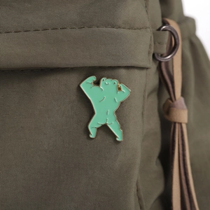 Macro shot of creative muscular frog enamel pin attached to a green nylon backpack fabric