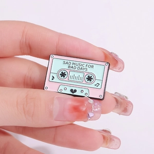 Retro cassette enamel pin featuring SAD MUSIC FOR BAD DAYS slogan in pink and green