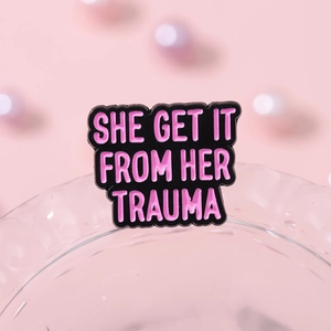Enamel pin with She Get It From Her Trauma text in pink lettering on black background