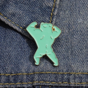 Detail of mint green muscular frog enamel pin attached to blue denim fabric texture