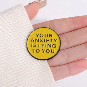 Pin's en émail jaune avec citation Your Anxiety Is Lying To You sur fond en maille blanc