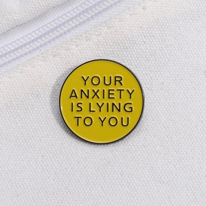 Détail du pin's émaillé jaune avec texte de motivation sur un sac en toile blanc