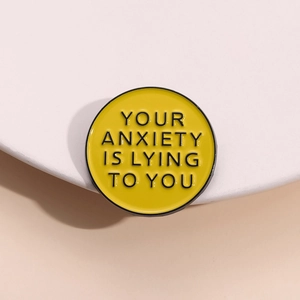 Gros plan du pin's rond en émail jaune avec la citation YOUR ANXIETY IS LYING TO YOU