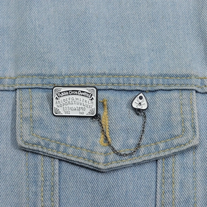 Détail d'un pin's gothique Ouija en émail avec chaîne sur une veste en jean bleue