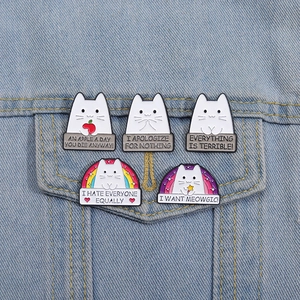 Detailed view of five creative white cat enamel pins on light blue denim fabric
