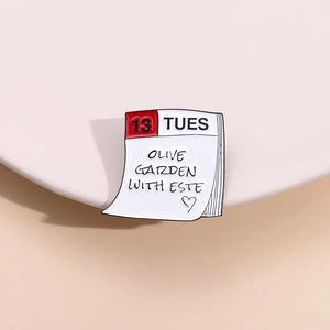 Detail of calendar enamel pin with Olive Garden text and minimalist aesthetic design