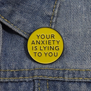 Broche en émail jaune avec texte YOUR ANXIETY IS LYING TO YOU sur tissu en denim