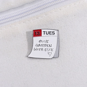 Detail of calendar enamel pin featuring Olive Garden with Este text on white canvas