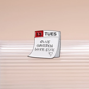White enamel calendar pin with red accents and hand-written style decorative text