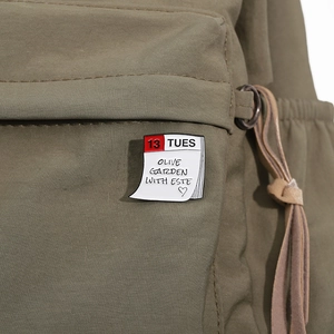 Macro detail of enamel calendar brooch with Olive Garden text on olive green canvas bag