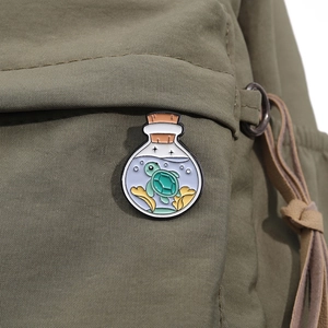 Detail of cute turtle in glass bottle enamel pin on a green canvas backpack surface