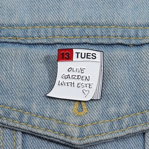 Macro shot of 13 Tuesday calendar enamel pin on denim, featuring Olive Garden text
