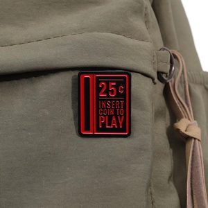 Close-up of retro arcade machine enamel pin on dark green canvas fabric texture
