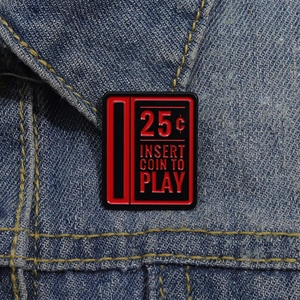 Close-up of retro 25 cent arcade coin slot enamel pin on a denim jacket collar