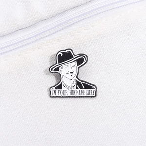 Detailed close-up of Doc Holliday enamel pin with I'm Your Huckleberry quote on white fabric