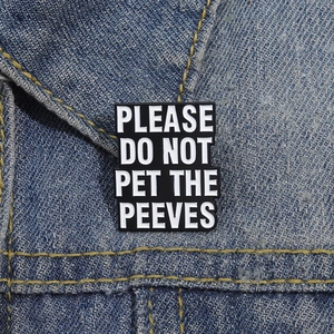 Close-up of enamel pin PLEASE DO NOT PET THE PEEVES on blue denim jacket fabric