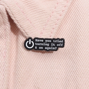 Détail du pin's en émail noir avec le texte 'Have you tried turning it off and on again?'