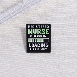 Detail of a rectangular black enamel pin featuring loading nurse text on canvas