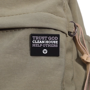 Detail of black Trust God enamel pin with inspirational text on green canvas bag