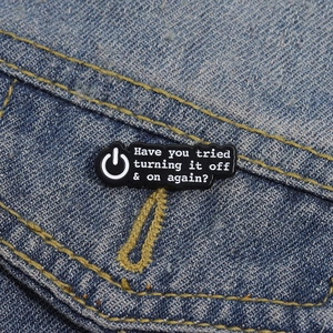Gros plan d'un pin's émaillé noir avec citation IT sur une poche de veste en jean