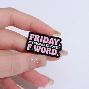 Black enamel pin with humorous Friday quote held by hand against gray background
