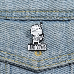 Détail du pin's émaillé rigolo 'I HATE EVERYONE' avec figurine de dessin animé sur denim