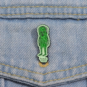 Funny green cucumber character enamel pin with a face on denim jacket fabric