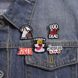 Detailed view of five unique enamel pins on a blue denim jacket with creative religious motifs
