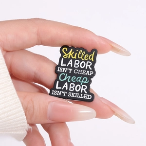 Schwarze Emaille-Brosche mit gelbem Spruch Skilled Labor Isn't Cheap in der Hand